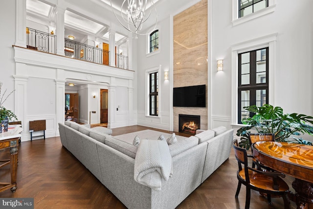 living room with a notable chandelier, a healthy amount of sunlight, dark parquet flooring, and a high ceiling