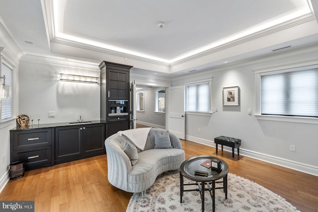 sitting room with light wood-type flooring, a tray ceiling, crown molding, and sink