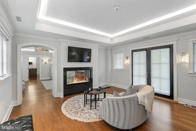 living room with wood-type flooring, a raised ceiling, french doors, and crown molding