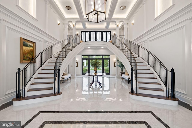 entrance foyer with coffered ceiling, a towering ceiling, crown molding, and french doors