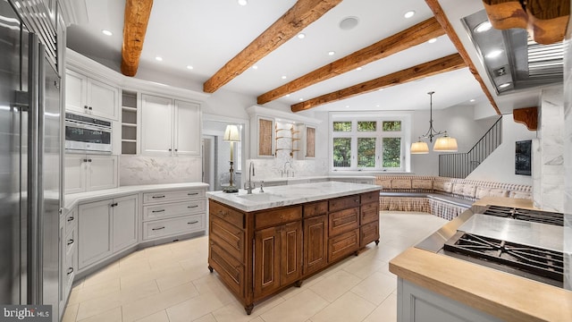 1717 Woodland Rd, Abington, PA 19001 - kitchen featuring an island with sink, appliances with stainless steel finishes, white cabinets, beamed ceiling, and tasteful backsplash