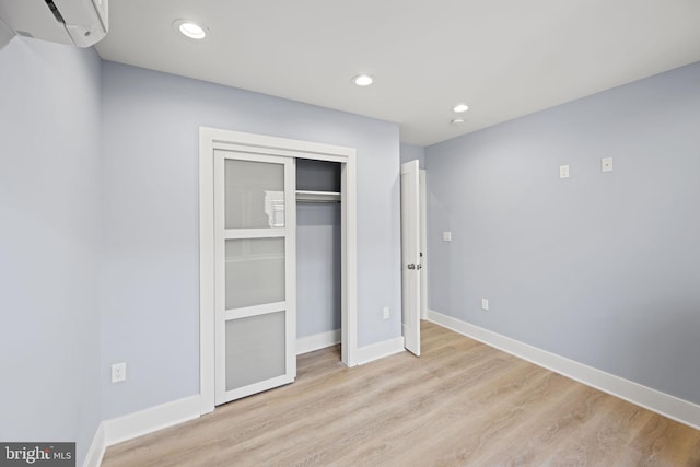 unfurnished bedroom featuring a closet, light hardwood / wood-style floors, and a wall mounted air conditioner