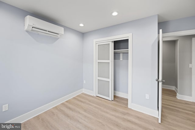 unfurnished bedroom featuring a closet, light hardwood / wood-style flooring, and a wall mounted air conditioner