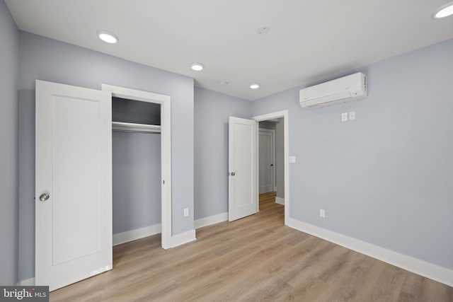 unfurnished bedroom with a closet, a wall unit AC, and light wood-type flooring