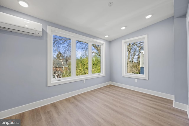 spare room with a wall mounted air conditioner, vaulted ceiling, and light wood-type flooring