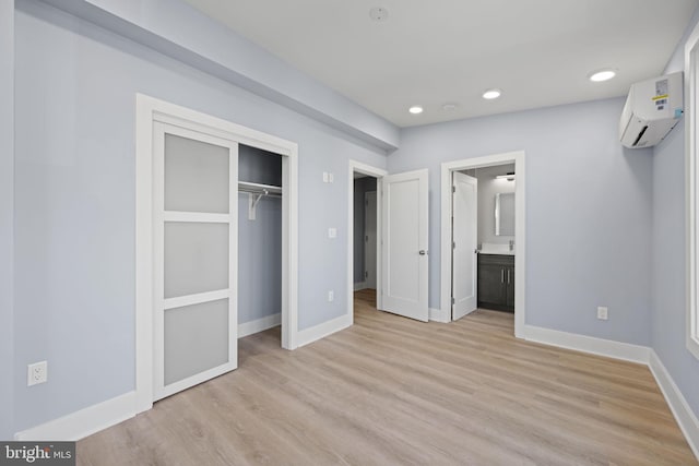 unfurnished bedroom featuring a closet, light hardwood / wood-style flooring, ensuite bath, and an AC wall unit