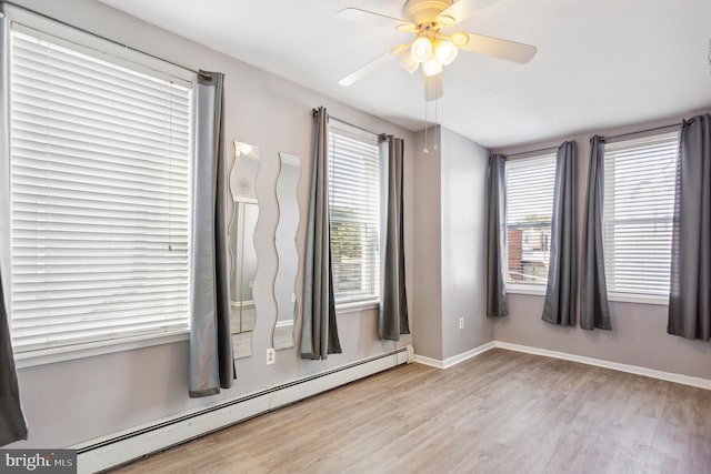 spare room featuring ceiling fan, baseboard heating, light hardwood / wood-style flooring, and a healthy amount of sunlight