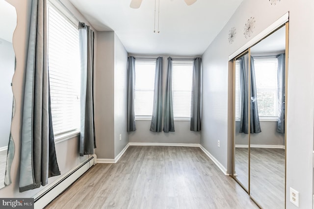 unfurnished bedroom with ceiling fan, baseboard heating, light wood-type flooring, and a closet