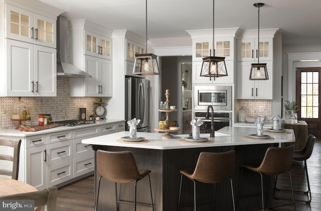 kitchen with wall chimney exhaust hood, decorative backsplash, appliances with stainless steel finishes, and dark wood-type flooring