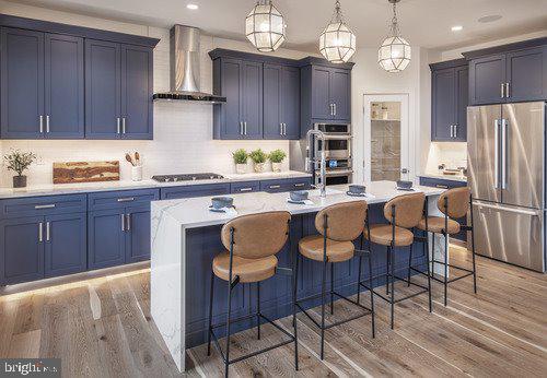 kitchen with a kitchen breakfast bar, hardwood / wood-style floors, appliances with stainless steel finishes, a center island with sink, and wall chimney range hood