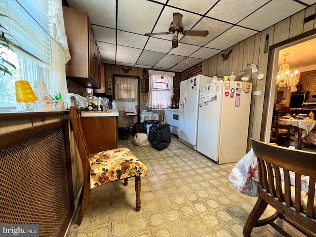 kitchen with ceiling fan with notable chandelier, white refrigerator, white refrigerator with ice dispenser, and wooden walls