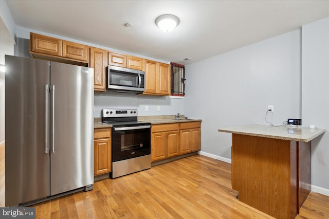 kitchen with light hardwood / wood-style flooring, stainless steel appliances, and kitchen peninsula