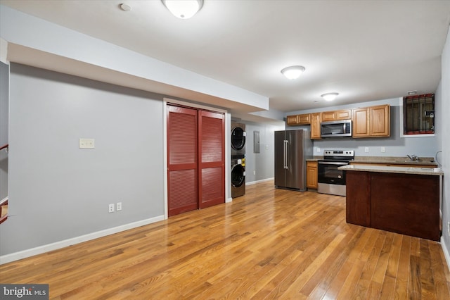 kitchen with stacked washing maching and dryer, light hardwood / wood-style floors, stainless steel appliances, and light stone countertops