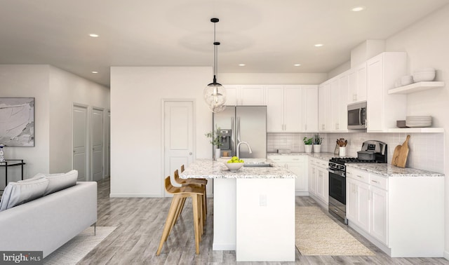 kitchen featuring pendant lighting, white cabinetry, light stone counters, a kitchen island with sink, and stainless steel appliances