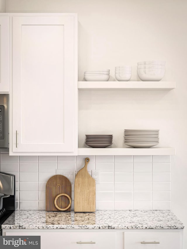 room details with light stone counters, backsplash, and white cabinets