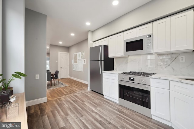 kitchen featuring white cabinets, light wood-type flooring, backsplash, and appliances with stainless steel finishes