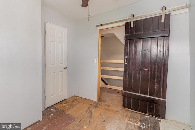 unfurnished bedroom with a barn door, ceiling fan, and hardwood / wood-style flooring