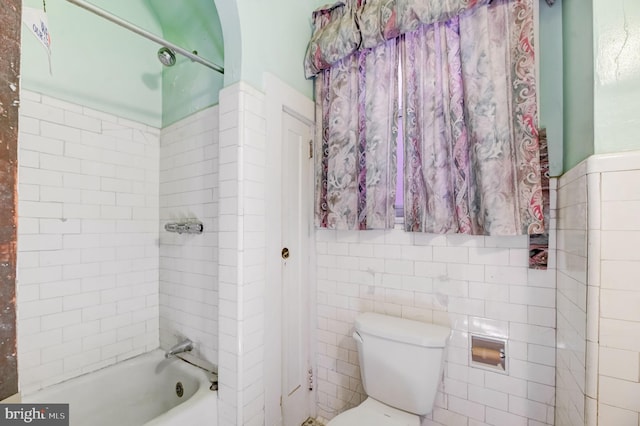 bathroom featuring toilet, tiled shower / bath combo, and tile walls