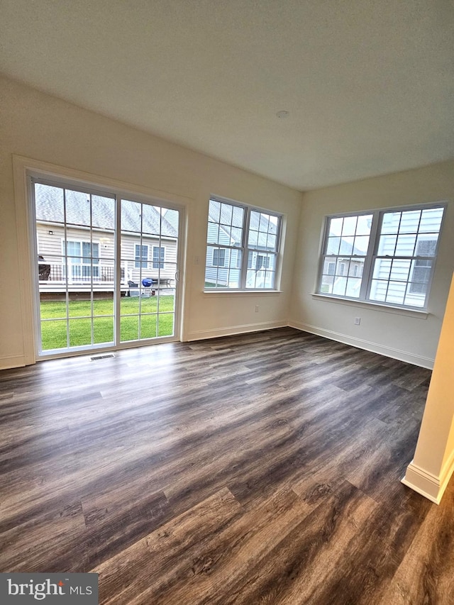 unfurnished room featuring a healthy amount of sunlight and dark wood-type flooring