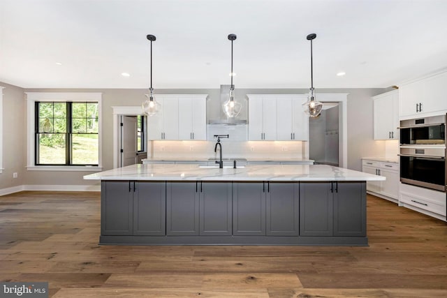 kitchen with double oven, a spacious island, light stone countertops, and white cabinets