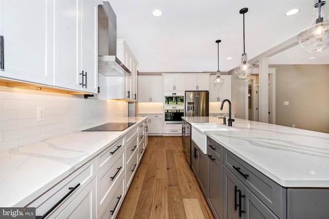 kitchen with hanging light fixtures, sink, white cabinets, and wall chimney exhaust hood