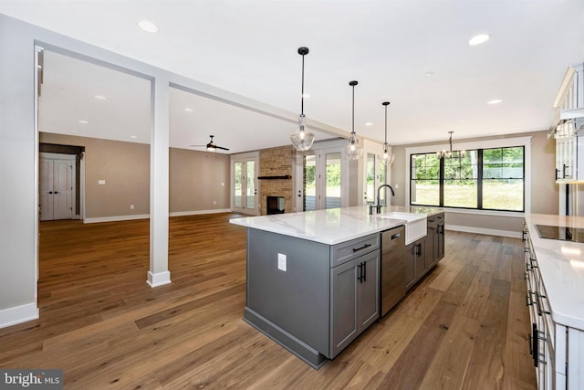 kitchen with gray cabinets, dishwasher, hanging light fixtures, a kitchen island with sink, and light stone countertops