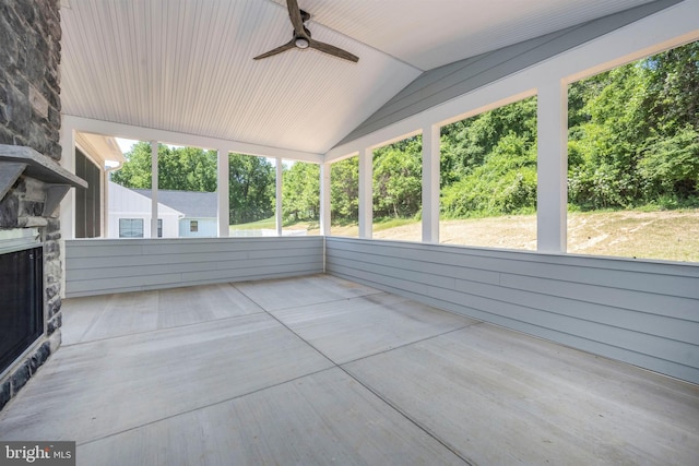 unfurnished sunroom featuring ceiling fan, a stone fireplace, and vaulted ceiling