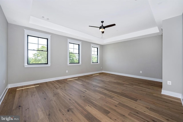 spare room with dark hardwood / wood-style flooring, a tray ceiling, and ceiling fan