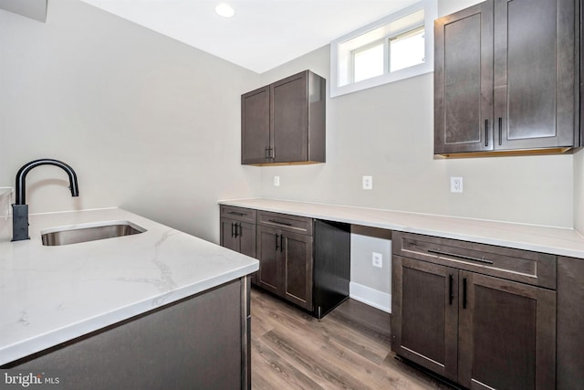 kitchen featuring sink, dark brown cabinets, light stone countertops, and light wood-type flooring