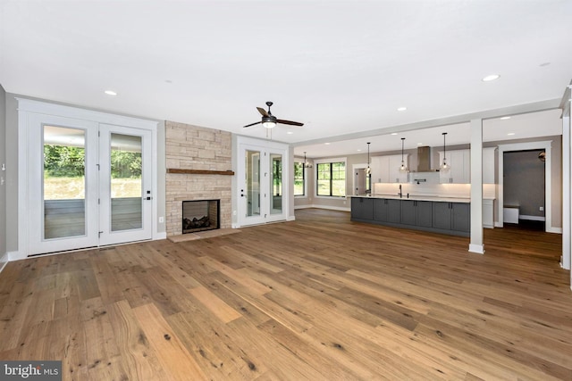 unfurnished living room featuring a stone fireplace, sink, hardwood / wood-style floors, and ceiling fan