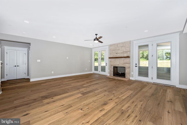 unfurnished living room with a stone fireplace, light hardwood / wood-style floors, french doors, and ceiling fan