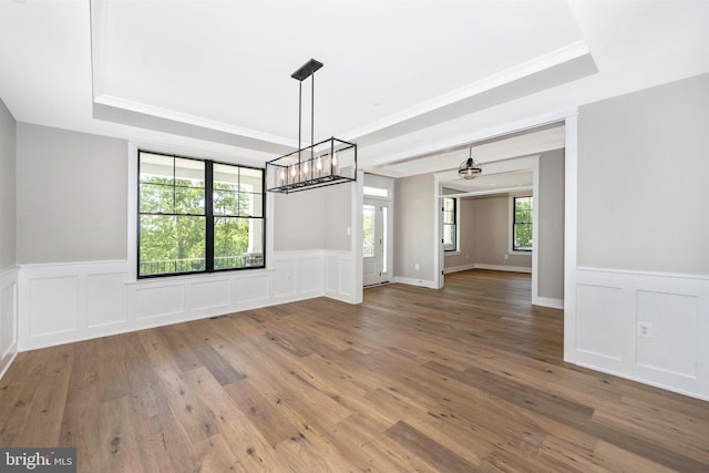 unfurnished dining area featuring crown molding, a tray ceiling, and wood-type flooring