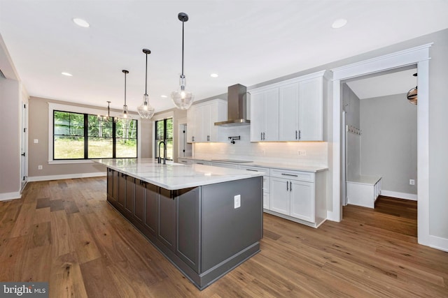 kitchen featuring wall chimney exhaust hood, black electric cooktop, a large island, decorative backsplash, and white cabinets