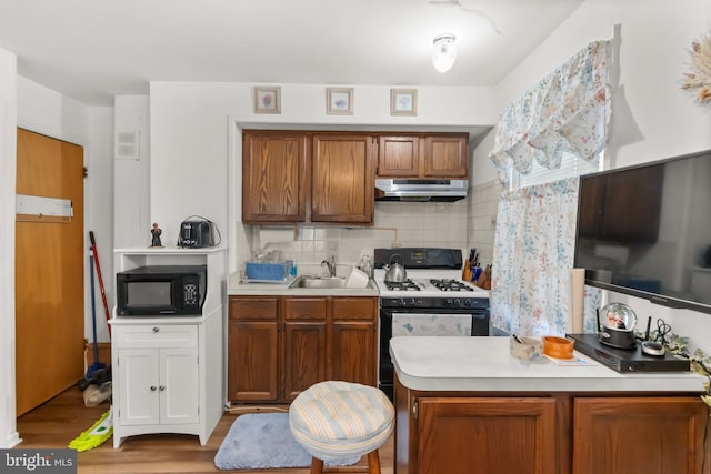 kitchen with white gas range oven, decorative backsplash, sink, and light hardwood / wood-style flooring