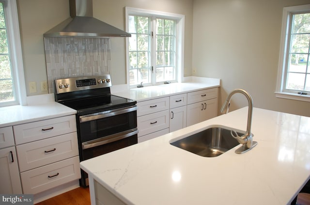 kitchen featuring a healthy amount of sunlight, light stone countertops, wall chimney exhaust hood, and stainless steel electric stove