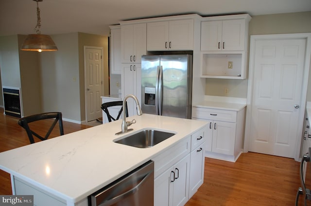 kitchen featuring light wood-type flooring, stainless steel appliances, decorative light fixtures, sink, and a kitchen island with sink