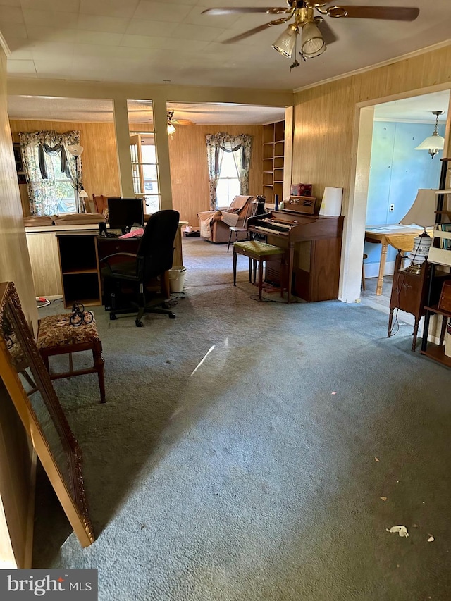 carpeted home office featuring wooden walls, crown molding, and ceiling fan