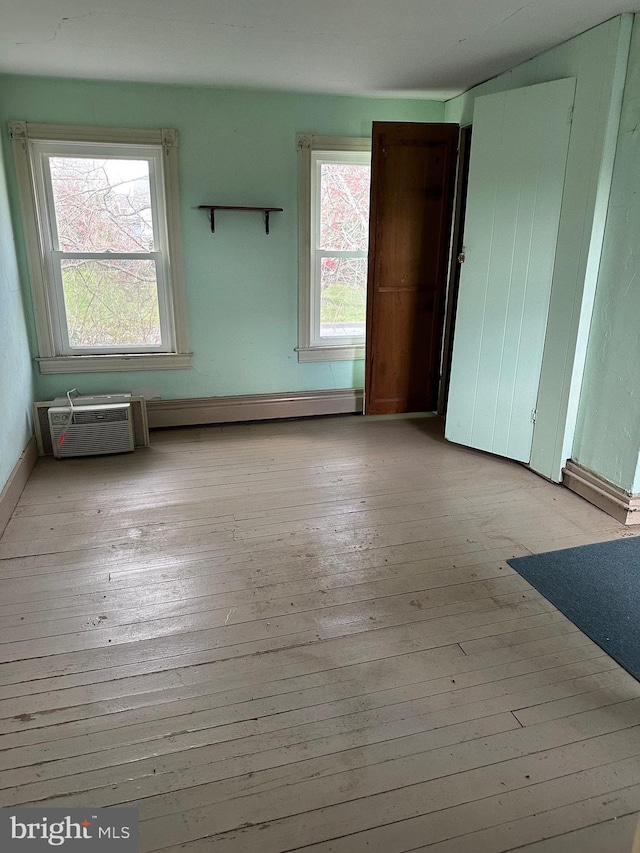 unfurnished room featuring a baseboard radiator, a wall mounted air conditioner, and light wood-type flooring