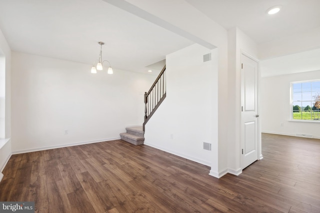 spare room featuring a chandelier and dark wood-type flooring