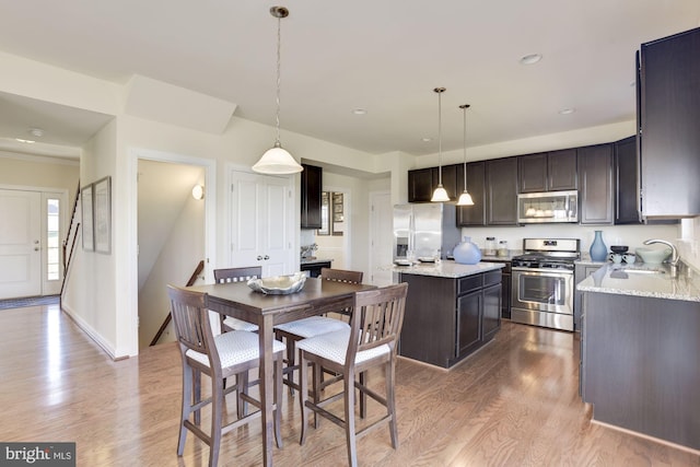 kitchen featuring sink, light hardwood / wood-style flooring, decorative light fixtures, and appliances with stainless steel finishes