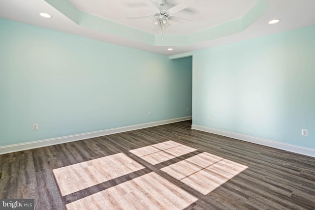 unfurnished room featuring a raised ceiling, ceiling fan, and dark hardwood / wood-style flooring