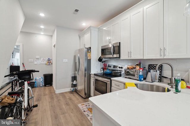 kitchen featuring stainless steel appliances, backsplash, light hardwood / wood-style floors, sink, and white cabinets