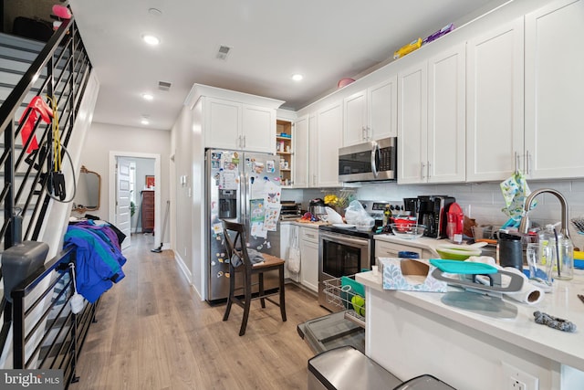 kitchen with white cabinetry, backsplash, light hardwood / wood-style floors, and stainless steel appliances