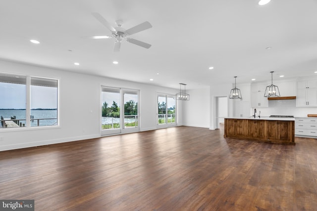 unfurnished living room featuring a water view, ceiling fan, dark hardwood / wood-style floors, and sink