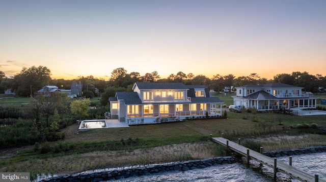 back house at dusk with a water view and a pool with hot tub