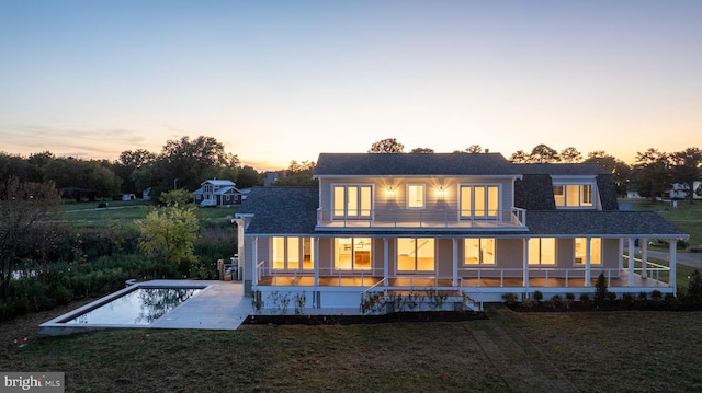 back house at dusk with a patio area, a yard, and covered porch