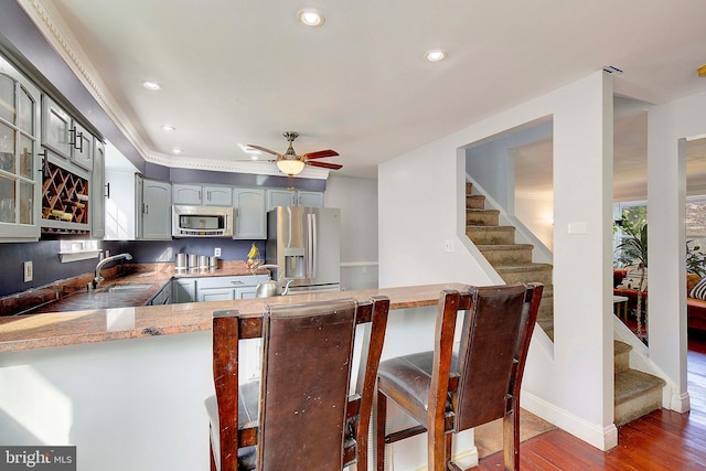 kitchen with kitchen peninsula, ceiling fan, gray cabinets, stainless steel appliances, and dark wood-type flooring