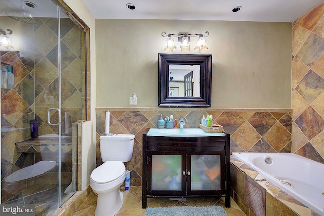 full bathroom with tile walls, toilet, vanity, and independent shower and bath