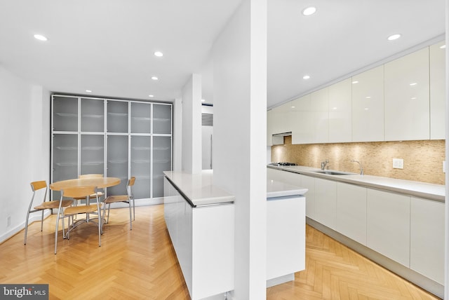 kitchen with white cabinets, light parquet floors, backsplash, and sink