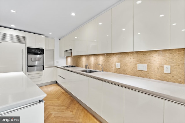 kitchen with sink, light parquet floors, backsplash, built in fridge, and white cabinetry